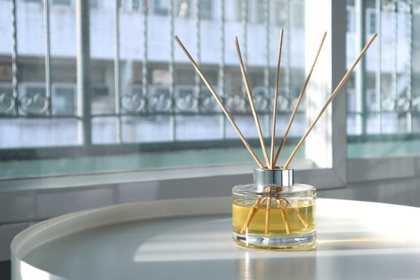 ylellinen aromaattinen tuoksu ruoko diffuusori lasipullo käytetään huoneen raikastin valkoinen metalli pöytä luoda rentoutua ja romanttinen ympäristö makuuhuoneessa ikkuna tausta illalla - Valokuva, kuva