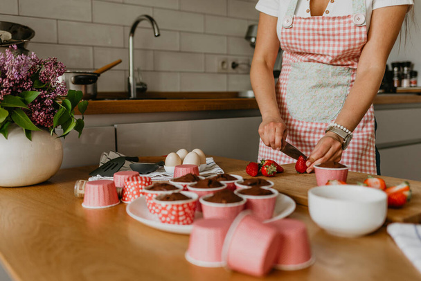 jonge vrouw versieren cupcakes in heldere keuken - Foto, afbeelding