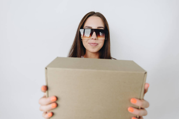Girl with glasses in focus. Portrait of a girl at a wide angle with a box in her hands. On a wide-angle lens, the concept of a box for goods - 写真・画像