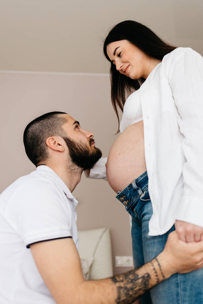 Handsome man is listening to his beautiful pregnant wife's tummy and smiling - Foto, afbeelding
