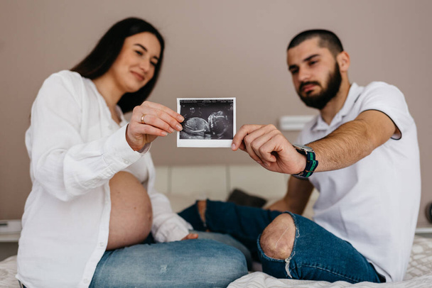 Immagine ritagliata di bella donna incinta e il suo bel marito con in mano un ecografo
 - Foto, immagini