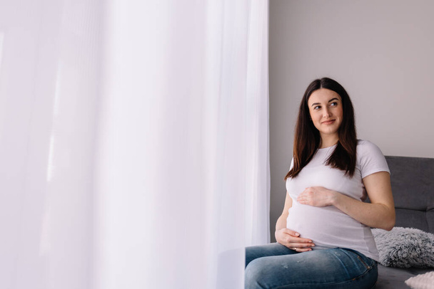 Nuori raskaana oleva nainen istuu ikkunassa
 - Valokuva, kuva