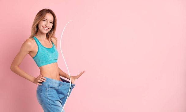 Happy young woman with slim body in oversized jeans on pink background, space for text. Weight loss - Fotoğraf, Görsel