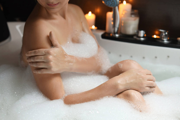 Woman taking bubble bath indoors, closeup. Romantic atmosphere - Zdjęcie, obraz