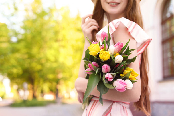 Teenage girl with bouquet of tulips on city street, closeup. Space for text - Foto, Imagen