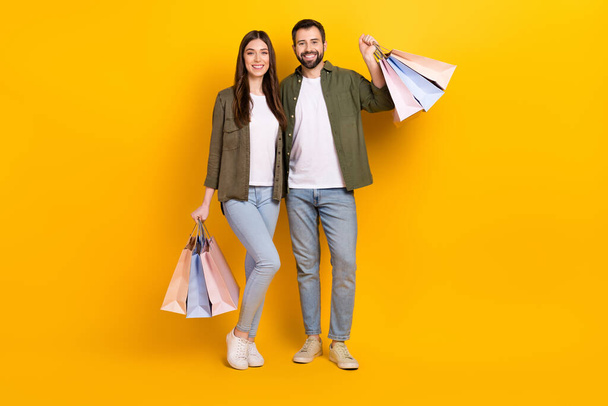 Full body photo of lovely couple hold shopping bags with stylish clothes isolated on yellow color background. - Фото, изображение