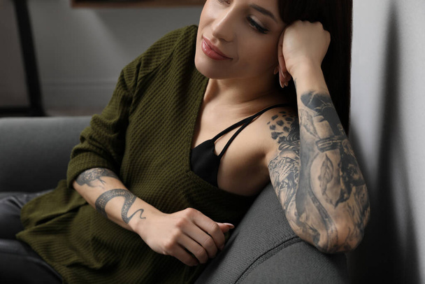 Beautiful woman with tattoos on arms resting in living room, closeup - 写真・画像