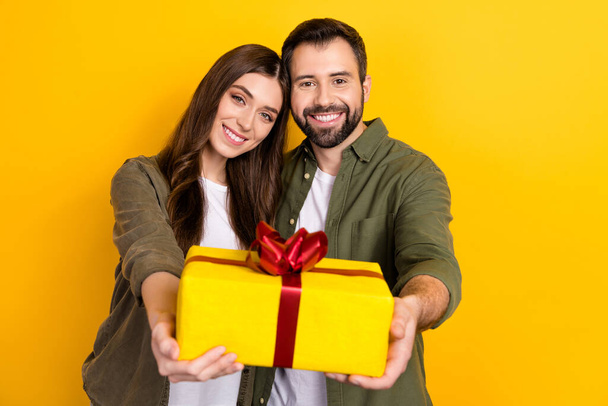 Photo of two idyllic positive people hold give you giftbox isolated on yellow color background. - Фото, изображение