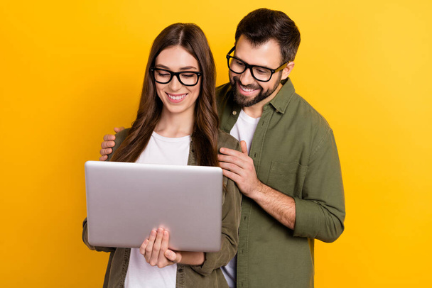 Photo of cute intelligent couple surfing in internet choose clothes buy stuff isolated on yellow color background. - Valokuva, kuva
