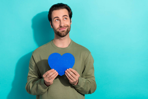 Photo of optimistic beard young guy hold heart look promo wear green sweatshirt isolated on turquoise color background. - Foto, Imagem