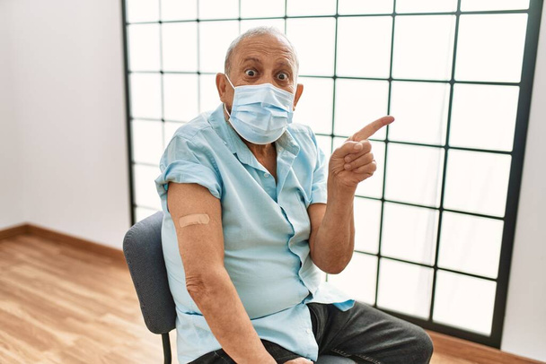 Mature hispanic man with grey hair getting vaccinated smiling happy pointing with hand and finger to the side  - Photo, Image