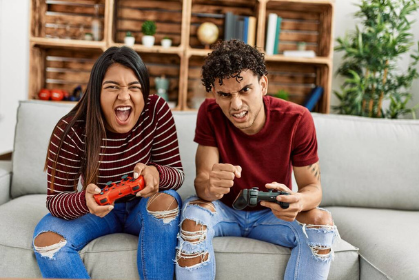 Young latin couple unhappy playing video game sitting on the sofa at home. - Foto, Imagen