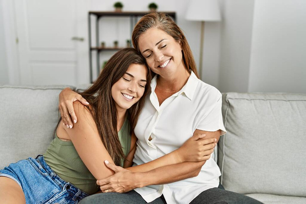 Mutter und Tochter lächeln selbstbewusst und umarmen sich auf dem heimischen Sofa - Foto, Bild