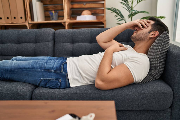 Young hispanic man stressed having mental therapy lying on sofa at psychology center - Фото, зображення