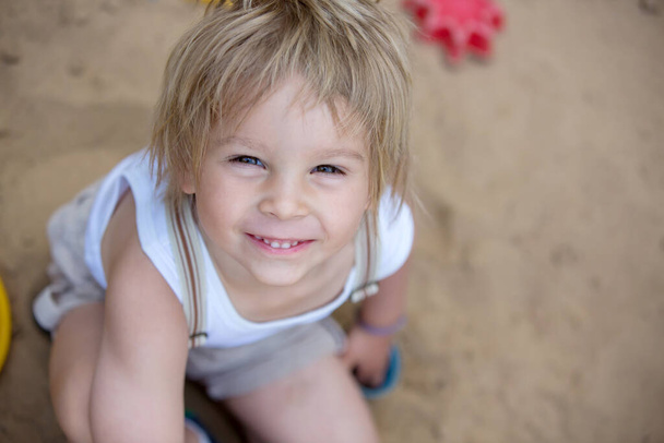 Tatlı çocuk, sarışın çocuk, yaz zamanı, parktaki kum havuzunda oynayan. - Fotoğraf, Görsel
