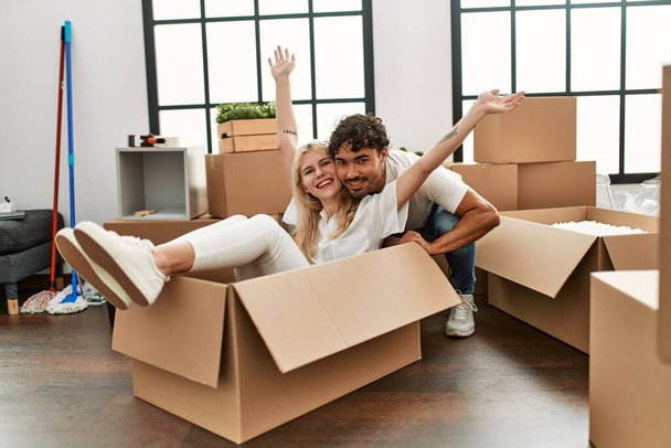Genç ve güzel bir çift mutlu bir şekilde yeni evlerinde karton kutuları araba olarak kullanıyorlar.. - Fotoğraf, Görsel