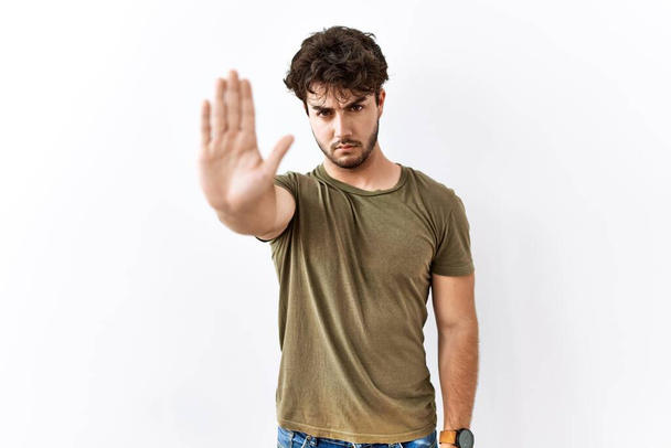 Hispanic man standing over isolated white background doing stop sing with palm of the hand. warning expression with negative and serious gesture on the face.  - Photo, Image