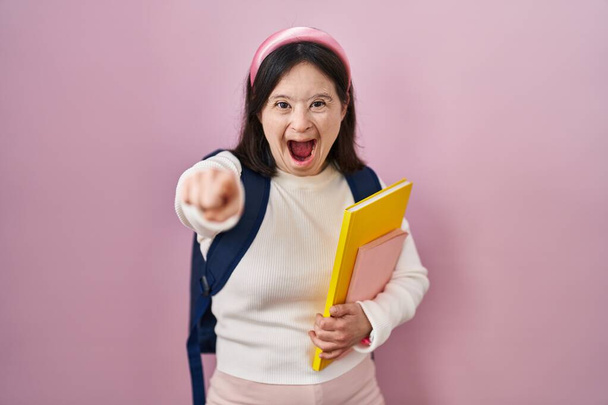 Nő Down-szindrómával visel diák hátizsák és a kezében könyvek rámutatva elégedetlen és frusztrált a kamera, dühös és dühös rád  - Fotó, kép