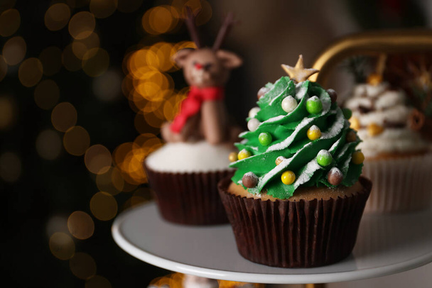 Christmas tree shaped cupcake on white stand against blurred festive lights, space for text - Valokuva, kuva
