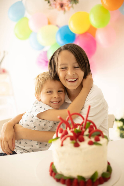 Cute child, preschool boy, celebrating birthday at home with homemade cake with raspberries, mint and candies, balloons and decoration in the room - Φωτογραφία, εικόνα
