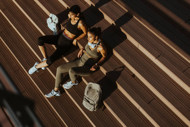 Por encima de la vista en las mujeres jóvenes y bonitas toma un descanso después de correr en el área urbana - Foto, Imagen