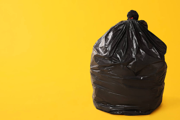 Trash bag full of garbage on yellow background. Space for text - Fotó, kép
