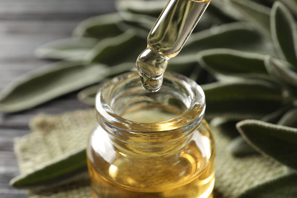 Dropping essential sage oil into bottle on blurred background, closeup - Фото, зображення