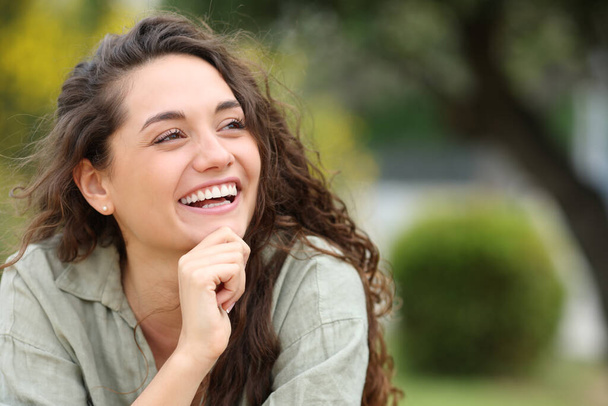 Happy beauty woman laughing sitting in a park looking at side - Foto, imagen