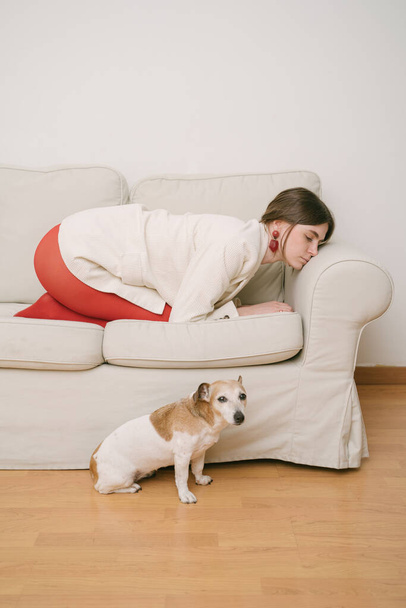 Woman curled up on beige sofa and dog on floor looking at camera. conceptual creative composition.  metaphorical expression to sad, avoid feelings and emotions. emotional burnout - Фото, зображення