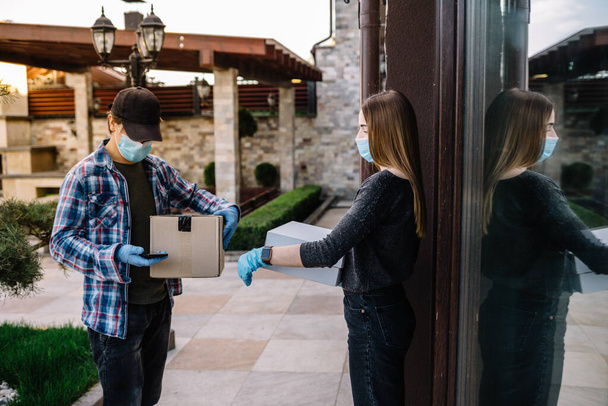 Женщина получает посылку от курьера у двери. медицинская маска, карантин - Фото, изображение