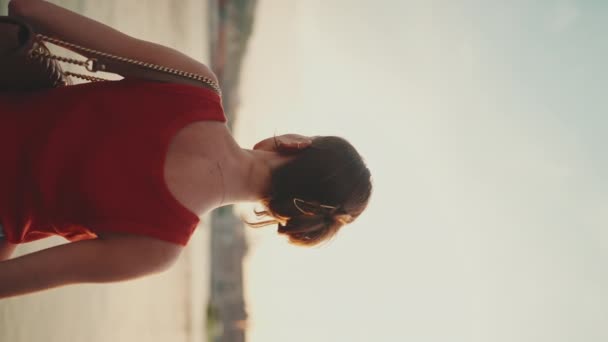 垂直方向のビデオ:クローズアップ、女の子は堤防の上に立って、湾を見ています。若い女性は午前中に海を見る。バックビュー - 映像、動画