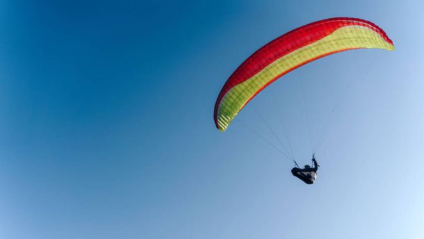 A paraglider in the blue sky. The sportsman flying on a paraglider. - Fotó, kép