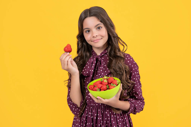 positive teen child hold strawberry bowl on yellow background. - Foto, Imagen