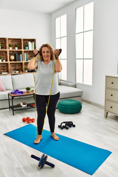 Middle age caucasian woman smiling confident training using elastic band at home - Photo, Image