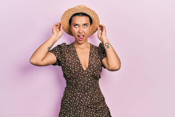 Beautiful hispanic woman with short hair wearing summer hat angry and mad screaming frustrated and furious, shouting with anger looking up.  - Foto, Imagem