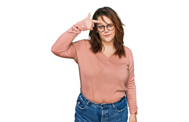 Junge Plus-Size-Frau in lässiger Kleidung und Brille, die unglücklich auf Pickel auf der Stirn deutet, hässliche Mitesser-Infektion. Akne und Hautprobleme  - Foto, Bild