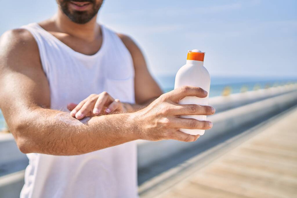 Hispanic sports man wearing workout style applying sunscreen on arm outdoors on a sunny day - Фото, зображення