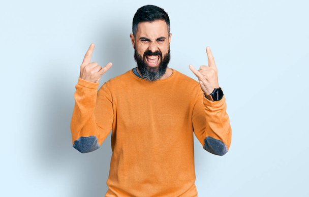 Hispanic man with beard wearing casual winter sweater shouting with crazy expression doing rock symbol with hands up. music star. heavy music concept.  - Valokuva, kuva