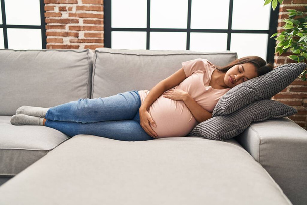 Young latin woman pregnant sleeping on sofa at home - Foto, Imagen