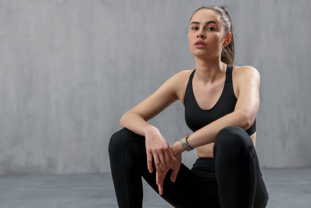 A young sporty woman in sports sitting against grey background, copy space - Fotó, kép