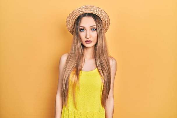 Young blonde girl wearing summer hat relaxed with serious expression on face. simple and natural looking at the camera.  - Foto, Bild