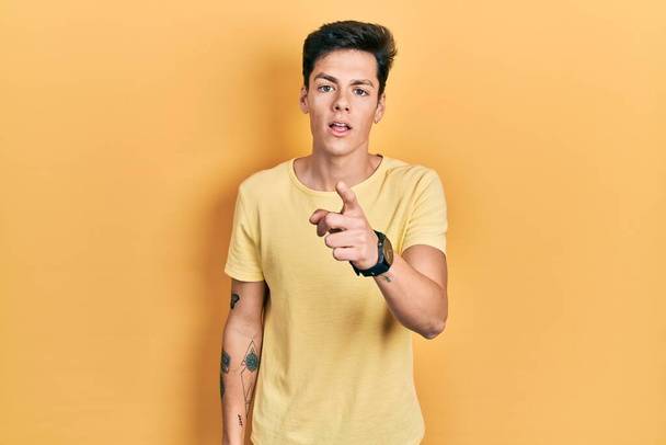 Jeune homme hispanique portant t-shirt jaune décontracté pointant mécontent et frustré à la caméra, en colère et furieux contre vous  - Photo, image