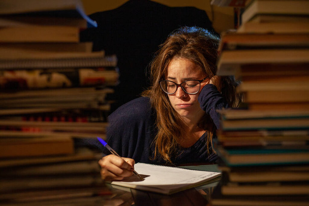 Zmęczona kobieta studiująca w bibliotece na egzaminy końcowe. - Zdjęcie, obraz
