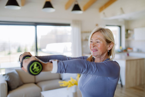 A fit senior woman exercising with dumbbells at home, active lifestyle concept. - Foto, afbeelding
