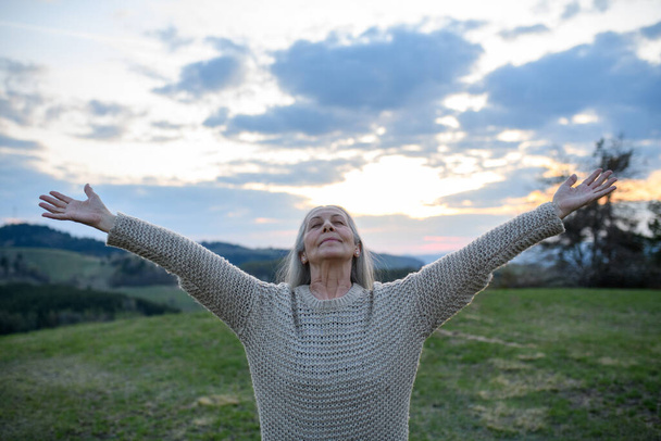 A senior woman with arms outstretched and face up at park on spring day - Fotoğraf, Görsel
