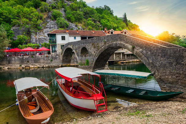 Ηλιοβασίλεμα πάνω από το Στάρι Μοστ και βάρκες στον ποταμό Κρνογιέβιτσα στο Μαυροβούνιο - Φωτογραφία, εικόνα