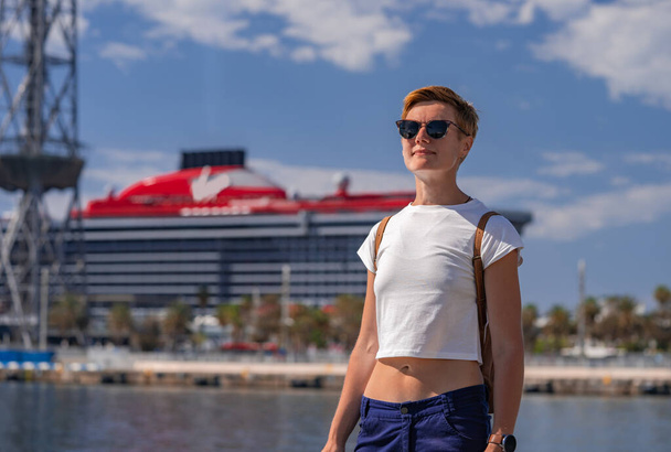Viaggiatore donna nel Port Vell con grande nave da crociera Virgin sullo sfondo. Barcellona, Spagna - 29 maggio 2022 - Foto, immagini