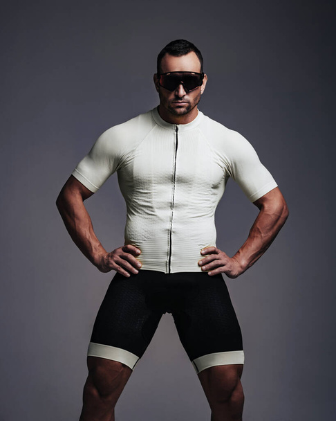 Fitnessmodel in Sportbekleidung zum Radfahren und Sonnenbrille im Studio - Foto, Bild