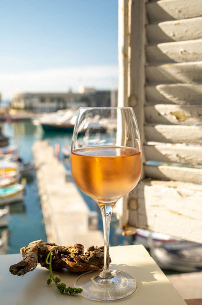 Rosa fría Vino provenzal en copa servido bajo la luz del sol en la terraza al aire libre con vistas al puerto de pescadores antiguos con barcos de colores en Cassis, Provenza, Francia - Foto, Imagen