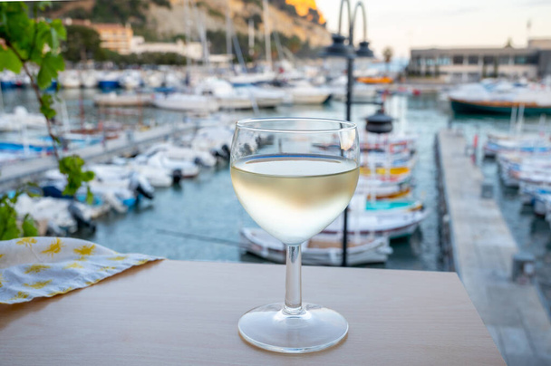Cold white wine from Cassis winemaking region served in glass on outdoor terrace with view on old fisherman's harbour with colourful boats in Cassis, Provence, France - Zdjęcie, obraz